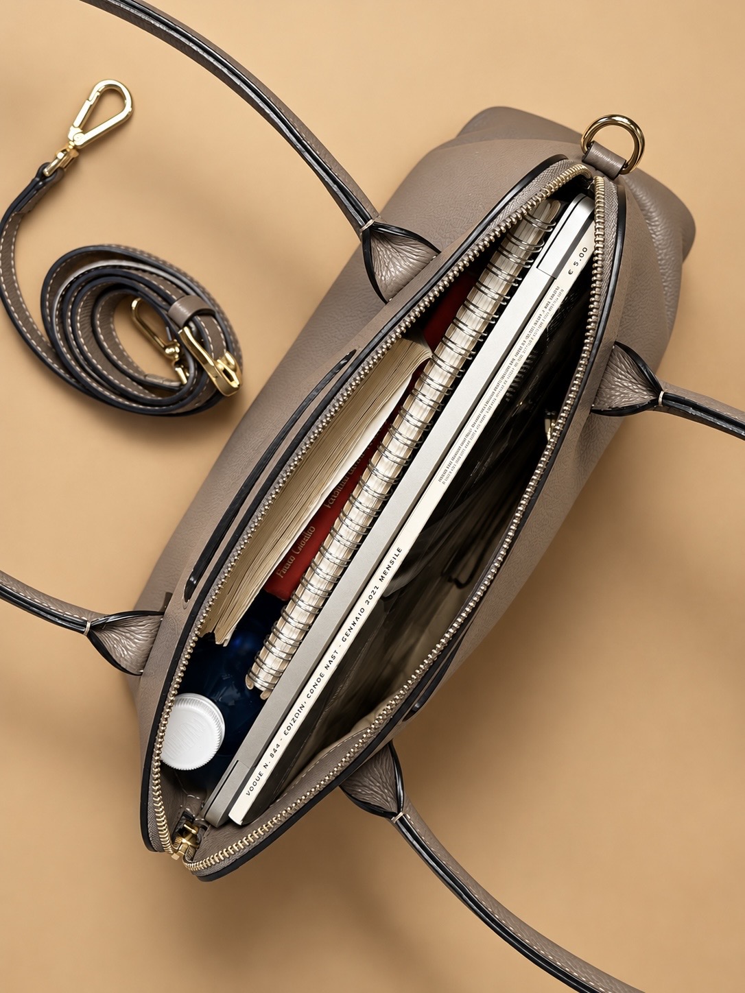 Borsa da lavoro Dalia Promenade IOEF in pelle martellata taupe, fotografata aperta dall’alto su fondo caramello, con agenda e accessori all’interno.