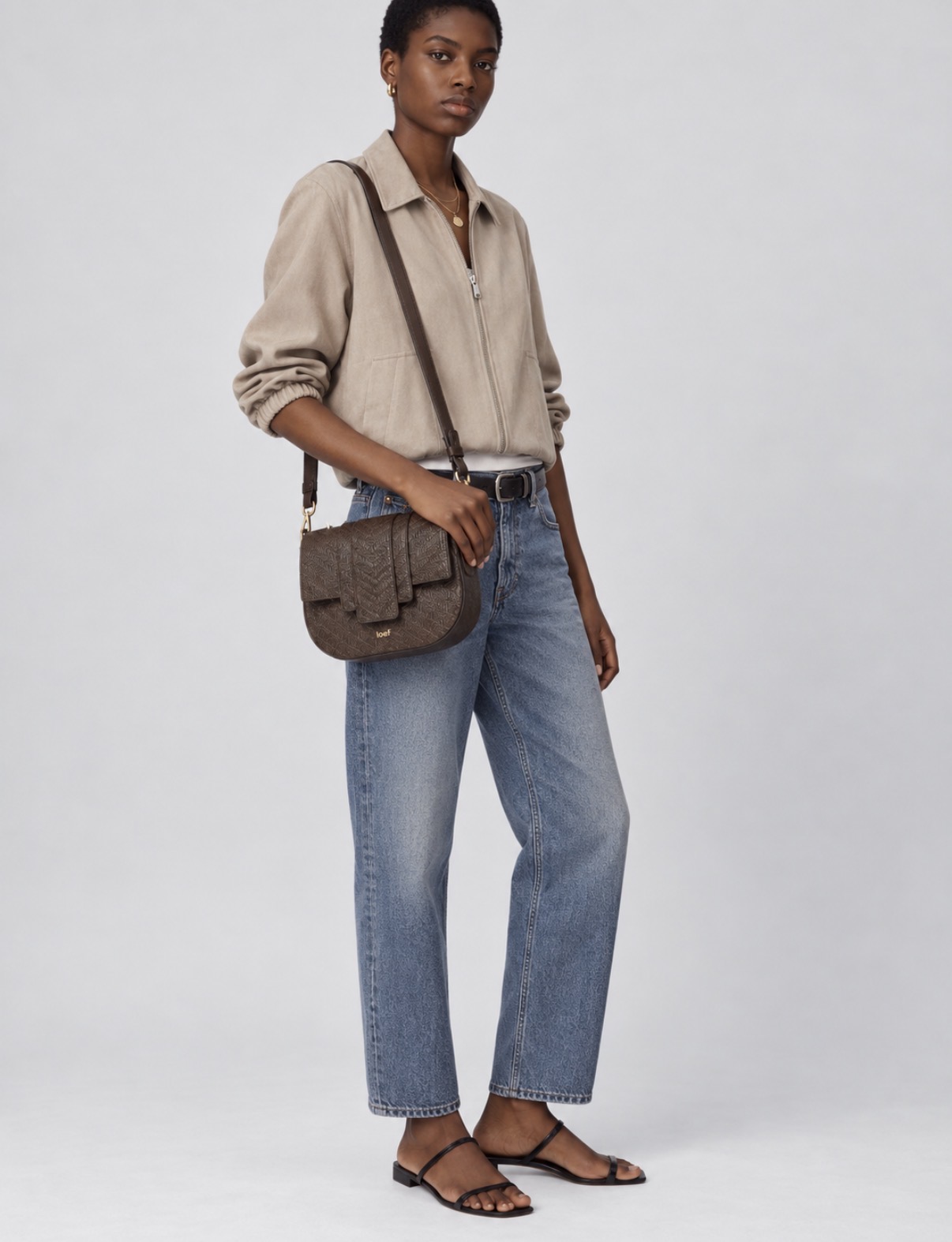 Modella con borsa a tracolla Kim IOEF in pelle stampa intreccio testa di moro, jeans e giacca beige